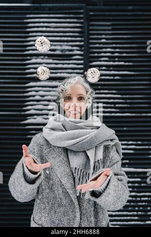 Femme souriante avec foulard gris jonglant boules Banque D'Images