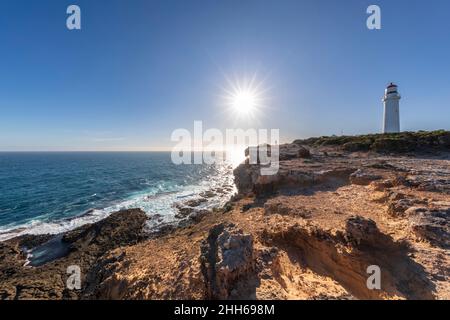 Australie, Victoria, soleil brillant sur la côte rugueuse du parc national de Cape Nelson avec le phare de Cape Nelson en arrière-plan Banque D'Images