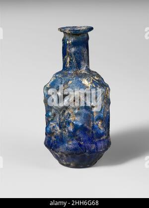 Bouteille hexagonale en verre ca.A.D. 25–50 Roman Translucent cobalt blueRim plié, rond, et dedans, puis pressé dans la bouche évasé; col cylindrique avec bande concave sous le bord; épaule inclinée vers le bas; corps hexagonal avec des côtés verticaux, puis en forme de cuvette en dessous; base basse avec bord arrondi et fond plat mais inégal.Les coutures de moule se trouvent près du haut du cou, sur les côtés, et se retrouvent excentré sur le fond.Décoration en relief dans trois registres : sur l'épaule, six rayons tournés vers le bas ou pétales pointés; sur le corps, six panneaux rectangulaires, chacun décoré en haut avec un fronton triangulaire, encadrés sur les côtés avec des poteaux Banque D'Images