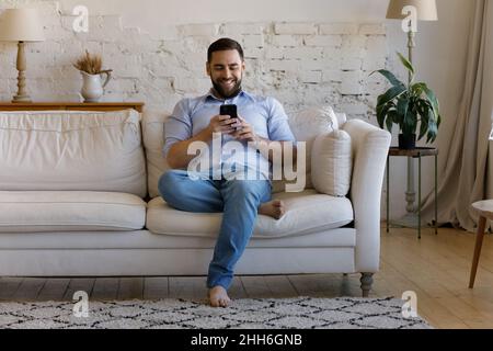 Joyeux utilisateur de smartphone bavardant en ligne, lisant des SMS Banque D'Images