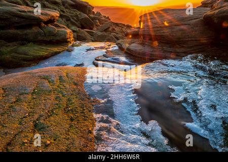 Glace sur la rivière Kinder à Kinder Downfall dans le Peak District, mettant le soleil au loin Banque D'Images