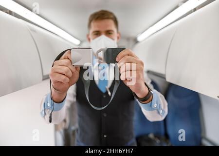 Un agent de bord masculin dans un masque facial de sécurité tenant la ceinture de sécurité Banque D'Images