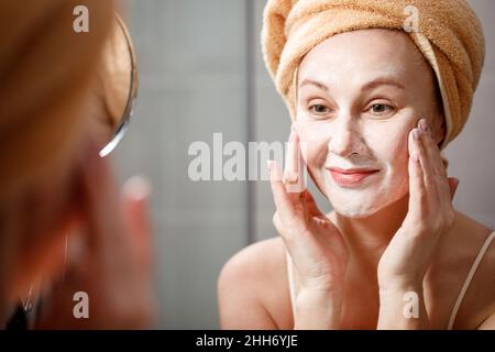 Une femme met un masque de nettoyage sur son visage dans la salle de bains devant le miroir.Soins de la peau.Soins de spa cosmétiques Banque D'Images