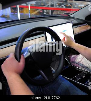 Conducteur masculin manipulant un écran tactile dans la cabine d'une voiture électrique. Banque D'Images