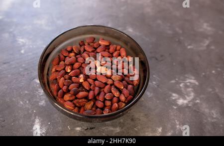 Arachides frites pelées, arachides pelées dans une plaque de verre blanc sur une table en bois sombre. Banque D'Images