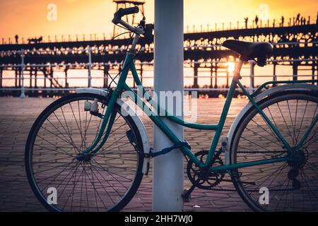 Avec le fond d'un coucher de soleil sur le quai Rio Tinto, un vélo d'époque reste attaché à un poteau à Huelva, Andalousie, Espagne Banque D'Images