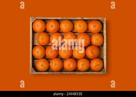 Caisse en bois de mandarines mûres sur fond orange. Mandarines de clémentine dans une boîte en bois. Vue de dessus. Convient à la création de répétitions sans couture. Banque D'Images