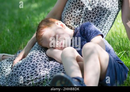 Les enfants dorment dans la nature.Un petit garçon dort sur les pieds de sa mère dans le parc. Banque D'Images