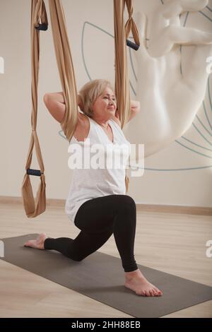 Prise de vue verticale en longueur d'une femme âgée qui s'étire avec un hamac de yoga aérien Banque D'Images