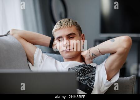 Portrait d'un jeune homme tatoué regardant des vidéos tout en se relaxant sur un canapé dans un appartement moderne Banque D'Images