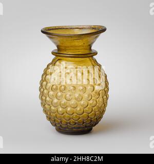 Pot en verre en forme de bouquet de raisins ca.3rd Century A.D. Roman, palestinien jaune verdâtre translucide.Rim replié, au-dessus et à l'intérieur, puis aplati dans la bouche; col en entonnoir; rouleau de projection creux au-dessus du col de l'épaule; corps ovoïde; base cylindrique basse, avec fond concave.Cicatrice Pontil au centre du fond.Corps soufflé dans un moule en trois parties de deux sections verticales, s'étendant de la base à l'épaule, et une section de base en forme de disque.sur le corps, un motif de raisins stylisés comprenant dix rangées de vingt-et-un boutons hémisphériques, et deux petites feuilles, pointant vers le bas et avec un ce Banque D'Images