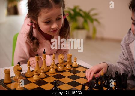 Gros plan d'une jolie petite fille européenne jouant au jeu d'échecs avec son frère aîné qui prend une pièce d'échecs et fait son mouvement.Int Banque D'Images