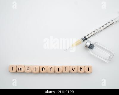 Lettres allemandes « Impfpflicht » pour « vaccination obligatoire avec seringue et flacon de vaccin isolé sur fond blanc Banque D'Images