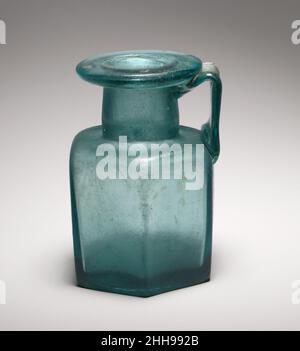 Flacon hexagonal en verre 2nd moitié de 1st–3rd Century A.D. Roman translucide bleu foncé vert ; poignée de la même couleur. Rebord replié, vers le bas, rond et intérieur, avec surface supérieure large et aplatie ;col cylindrique mais légèrement convexe, avec de légères marques d'outillage horizontales autour de la base ; épaulement horizontal légèrement dentelé avec coins arrondis ; corps hexagonal avec côtés plats légèrement inclinés vers le bas ; fond épais et plat ;Large poignée de sangle, peignée sur la surface extérieure, appliquée comme un long coussin sur le bord de l'épaule, tracée verticalement, puis courbée vers l'intérieur et vers le bas, et attachée au cou avec une traînée vers le haut.sur le fond, Banque D'Images