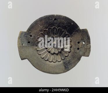 Fragment de couvercle ca.9th–8th siècle av. J.-C. Assyrian ce morceau brisé d'ivoire sculpté était probablement un couvercle pour une petite boîte ronde, appelée pyxis par des chercheurs.Environ un quart du couvercle a été restauré après l'excavation de l'objet et peut être distingué de l'objet ancien par sa couleur uniforme et sa texture de surface.La surface supérieure du couvercle est décorée d'une rosette centrale avec deux rangées concentriques de pétales.Le couvercle a probablement été fixé à sa boîte par des chevilles placées à travers les trous percés à travers les deux languettes symétriques projetant du bord, ce qui permet au couvercle de pivoter ouvert quand un Banque D'Images