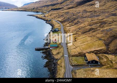 Une route sinueuse dans les îles Féroé embrasse le front de mer et passe devant les maisons traditionnelles vertes et rouges. Banque D'Images