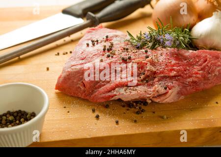 Essayez une pointe de bœuf sur une planche à découper en bois de bouchers avec du romarin frais, de la sauge, de l'oignon, de l'ail, du poivre et de l'assaisonnement. Couteau de chef et acier aiguisé. Banque D'Images