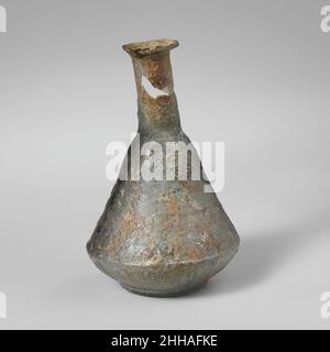 Flacon de parfum en verre mi-1st Century A.D. Roman translucide bleu pâle vert. Rebord replié, au-dessus et à l'intérieur, s'étendant dans le cou d'un côté de la bouche; corps sculpté, avec face supérieure droite conique et face inférieure courbé en relief sur le disque de base surélevé;Fond plat avec bouton central enfoncé.lignes horizontales en relief autour du haut du corps; garroons surélevés sur le bas du corps; deux cercles concentriques surélevés sur le bas.cassé autour du bord et du cou, avec une grande partie du cou manquante; piqûres profondes et intempéries irisées.Flacon de parfum en verre.Romain. Milieu–1st siècle A.D..Verre ; moulé.Début de l'Impériale. Banque D'Images