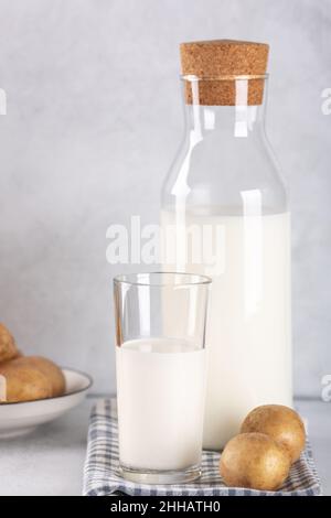 Boisson de pomme de terre sans lait en verre et en bouteille.Lait de pomme de terre de remplacement et tubercules de pomme de terre sur table grise.Copier l'espace Banque D'Images