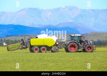 Un tracteur et une presse à foin travaillant dans un champ agricole dans la campagne de Canterbury, en Nouvelle-Zélande Banque D'Images