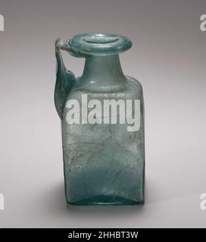 Flacon carré en verre 1st–3rd Century A.D. Roman bleu translucide, avec manche de même couleur.large, rebord épais plié, vers le bas, sur et vers l'intérieur, et lissé en haut de la bouche; col cylindrique, extensible vers le bas; épaule inclinée avec coins arrondis, inclinés; côtés plats, verticaux; épais,fond concave avec grande cicatrice de pontil ;Large poignée de sangle, avec décoration peignée sur la surface extérieure, fixée à l'épaule et au haut du corps dans un long coussin épais, dressé verticalement, tourné en angle aigu et traîné sur le cou, avec le sentier s'étendant sur le dessous de la jante.décoration moulée sur le fond comprenant i Banque D'Images