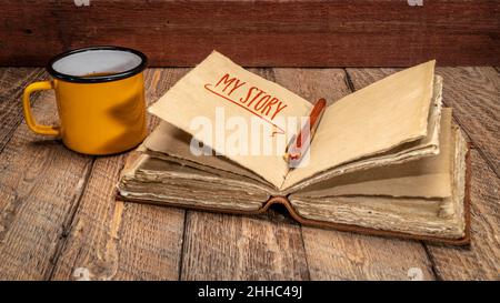 mon histoire - écriture dans un journal rétro en cuir lié avec des pages de papier à la main à bord incliné et une tasse de thé sur bois rustique, concept de journalisation Banque D'Images