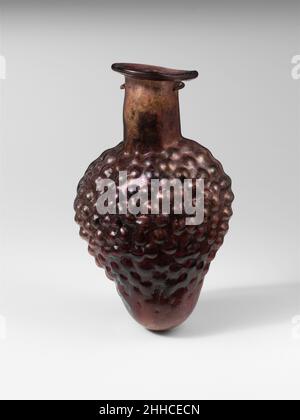 Bouteille en verre en forme d'un bouquet de raisins 1st Century A.D. Roman violet translucide.Rim plié, rond, et dedans, et pressé dans la bouche ovale oblique; col cylindrique avec côtés concave; corps légèrement lentoïde; fond rond.Un joint de moule continu autour du corps, mais visible uniquement sur les côtés.corps moulé en forme de petit bouquet de raisins ronds.grand trou dans le fond; quelques bulles; légère morcellement et piqûres sur l'extérieur, incrustation de sol, épaisse altération noirâtre et éclat brillant à l'intérieur.Bouteille en verre en forme de bouquet de raisins.Romain.1st siècle A.D..Verre ; soufflé Banque D'Images