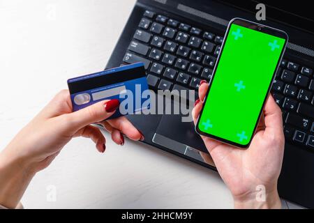 Gros plan des mains de femme utilisant un smartphone écran vert vierge maquette et tenant la carte de crédit Banque D'Images