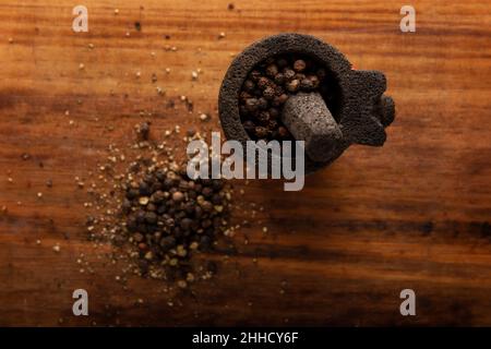 Grains de poivre noir dans un petit Molcajete (version mexicaine traditionnelle du mortier et du pilon) sur fond de bois rustique.Image de Flat lay.Gros plan Banque D'Images