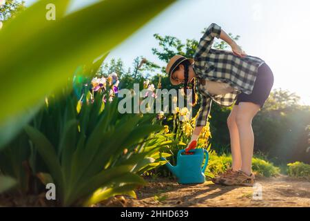 La femme caucasienne se tient pendue près d'un arbuste à iris en fleurs, la tenant dans la douleur.Vue de dessous.Le concept des problèmes de santé de dos. Banque D'Images