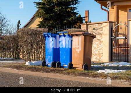 Trois bacs de recyclage en plastique pour le tri des déchets devant une petite maison dans un village Banque D'Images