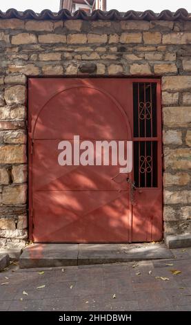 Porte métallique rouge avec treillis fermée sur la chaîne avec serrure dans le vieux mur en pierre. Banque D'Images