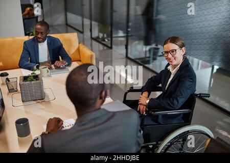 Portrait d'une femme d'affaires réussie utilisant un fauteuil roulant lors d'une réunion et parlant à un groupe de collègues dans un espace de bureau moderne Banque D'Images