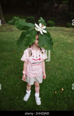 Petite fille en t-shirt rose avec une grande fleur blanche sur sa tête.Printemps. Banque D'Images