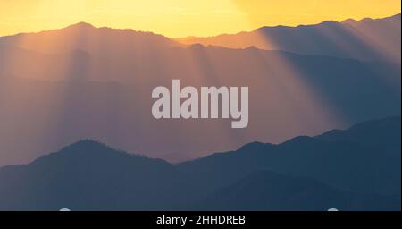 Ciel spectaculaire au coucher du soleil avec lumière orange qui brille sur des couches sombres de la chaîne de montagnes. Banque D'Images