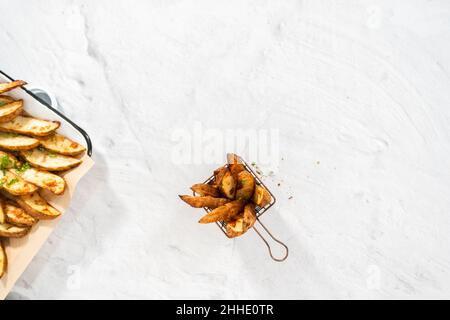 Pose à plat. Quartiers de pommes de terre fraîchement cuits avec épices dans un panier en fil métallique. Banque D'Images