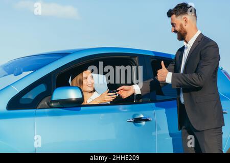 un homme remet les clés de la voiture à une femme assise dans la voiture Banque D'Images