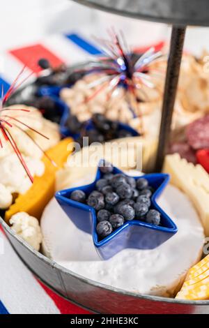 Le 4 juillet, un plateau de charcuterie est servi sur un support métallique à deux niveaux rempli de fromage, de craquelins, de salami et de fruits frais Banque D'Images