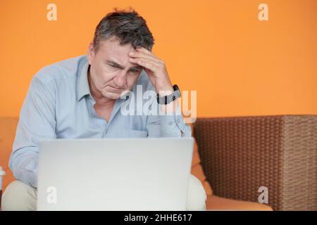 Un entrepreneur senior pensif stressé lisant un document important sur l'écran d'un ordinateur portable Banque D'Images