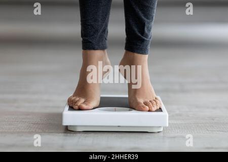 Jeune femme indienne méconnaissable qui vérifie son poids, debout sur des balances à l'intérieur, gros plan des pieds Banque D'Images