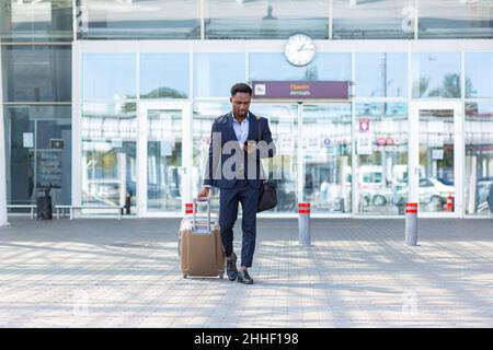 homme d'affaires africain voyageant près de l'aéroport avec une valise appelant un taxi à l'aide de l'application mobile Banque D'Images