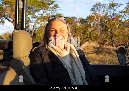 Une femme âgée souriante assise dans une jeep au coucher du soleil, souriante. Banque D'Images