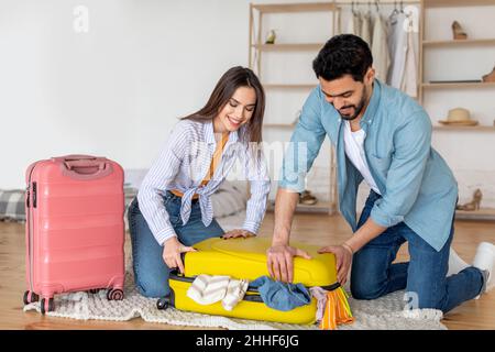 Jeune couple essayant de fermer plein de valise de vêtements, se préparant pour les vacances et emballer des choses ensemble à la maison Banque D'Images