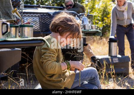 Garçon de 8 ans assis près de véhicules de safari, delta d'Okavango, Botswana Banque D'Images
