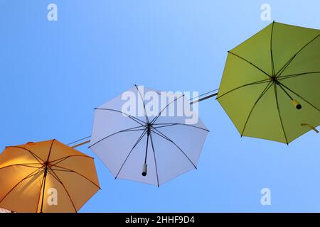 Parasols orange, blanc et jaune suspendus au ciel bleu clair de l'été Banque D'Images