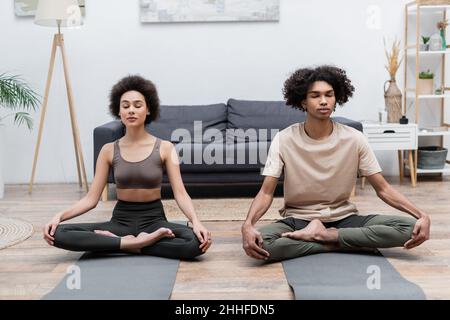 Jeune couple afro-américain méditant sur des tapis de yoga à la maison Banque D'Images