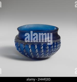 Bol à côtes en verre mi-1st Century A.D. Roman bleu cobalt translucide ; traînée en blanc opaque.renfoncée, rebord inégal; cou concave profond; épaule étroite inclinée; corps globulaire accroupi courbé à fond plat.enroulement de sentier épais en spirale autour du fond, puis de plus en plus fin lorsqu'il continue sur le côté, se terminant sur le bord de l'épaule;Côtés en vingt-quatre côtes verticales, espacées de manière inégale. Intactes; piqûres et bulles allongées; mordillements, piqûres légères, faible iridescence, et altération de la traînée autour des côtes.les bols nervurés comme ceux-ci, souvent décorés de sentiers blancs opaques, étaient très p Banque D'Images