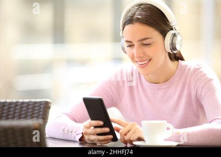 Bonne femme portant un casque vérifiant que le smartphone écoute de la musique dans un bar Banque D'Images