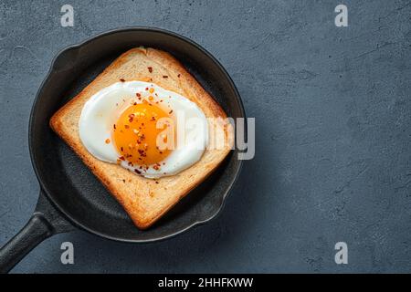 Les œufs frits sur du pain grillé dans une poêle sur fond sombre. Banque D'Images