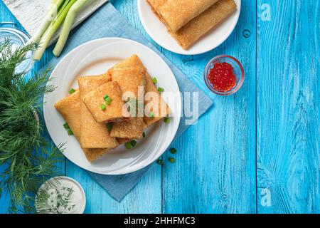 Crêpes farcies au caviar rouge, crème aigre et herbes fraîches sur fond bleu Banque D'Images